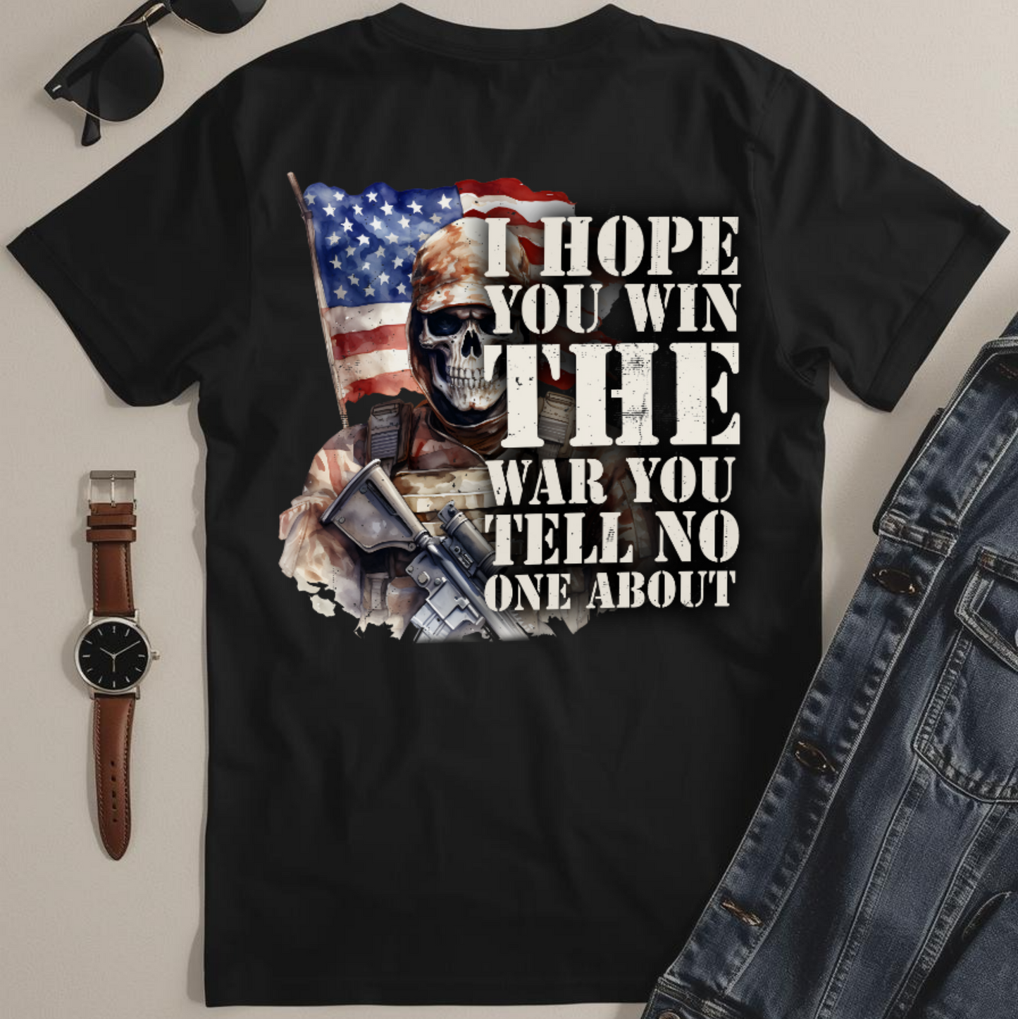 Black t-shirt with graphic design and text, sunglasses, watch, and jeans on a light gray background