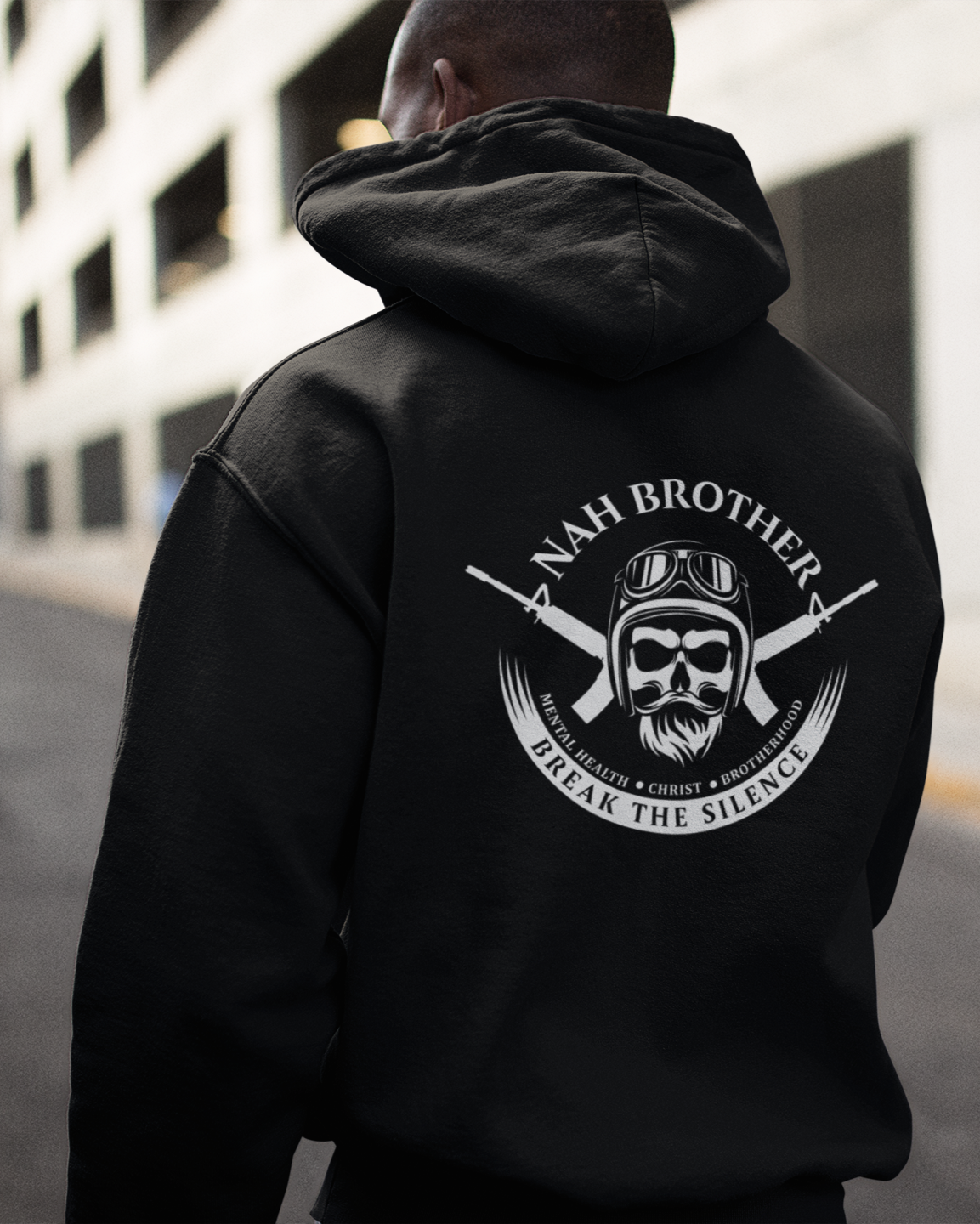 Person wearing a black hoodie with a logo and text on the back, standing in an urban setting.