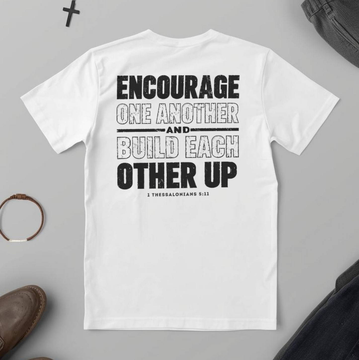 White t-shirt with motivational quote on a gray surface with accessories.