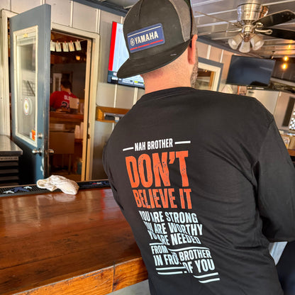 Person wearing a black shirt with text, standing in a room with wooden floor and furniture.