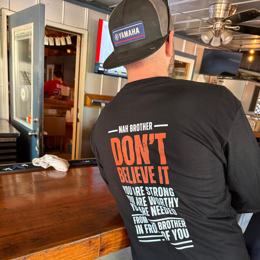Person wearing a black shirt with text, standing in a room with wooden floor and furniture.