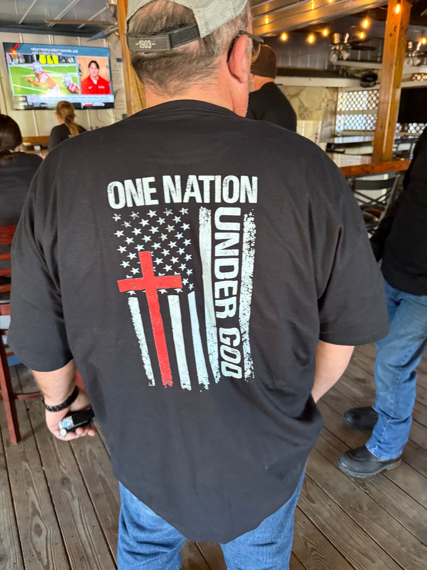 Person wearing a black t-shirt with a design featuring 'One Nation Under God' and an American flag.
