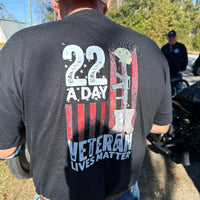 Person wearing a black t-shirt with '22 A Day Veteran Lives Matter' design outdoors.