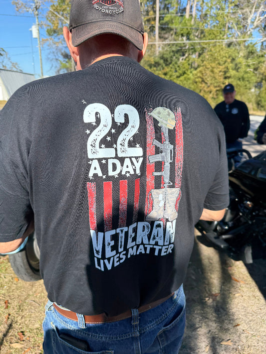Person wearing a black t-shirt with '22 A Day Veteran Lives Matter' design outdoors.