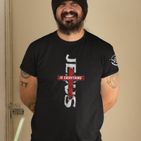 Man wearing a black t-shirt with 'Jesus is Everything' design against a beige wall.