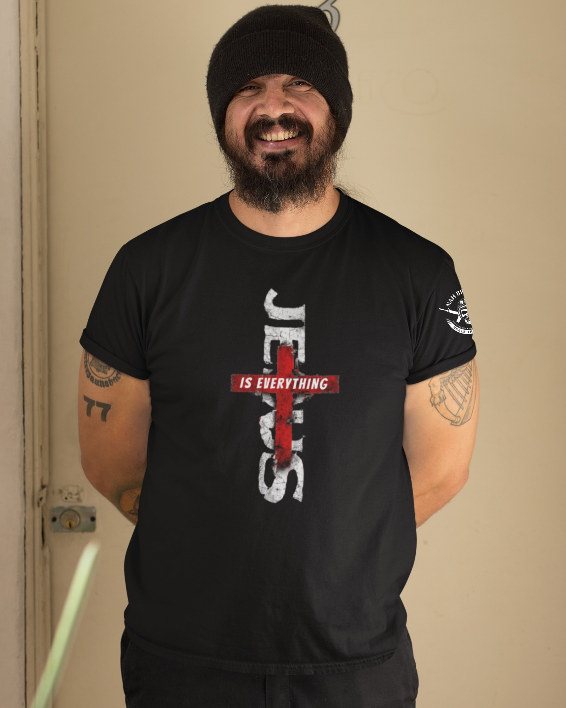 Man wearing a black t-shirt with 'Jesus is Everything' design against a beige wall.