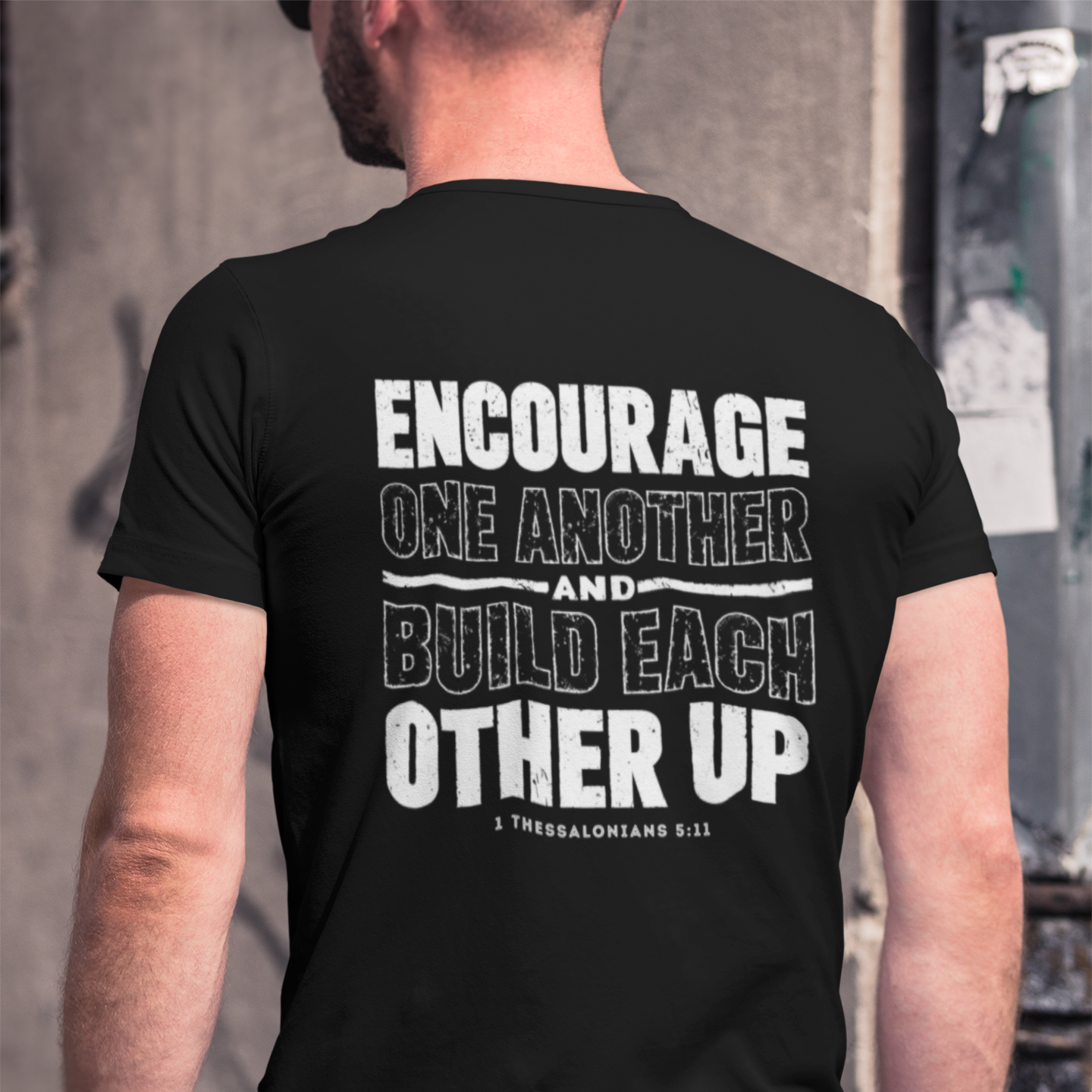 Person wearing a black t-shirt with motivational quote on the back, standing against an urban background.