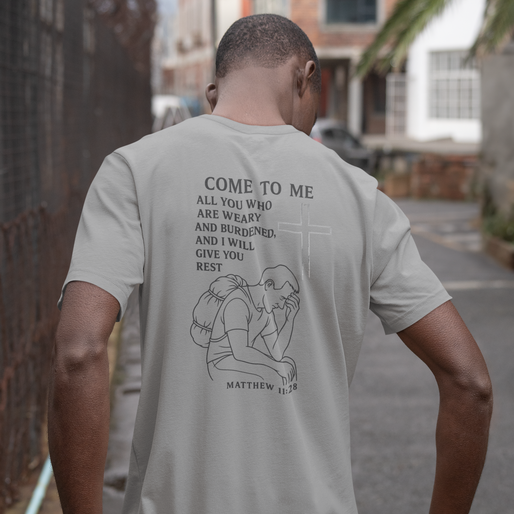 Man wearing a light gray t-shirt with text and graphics on the back, standing outdoors.