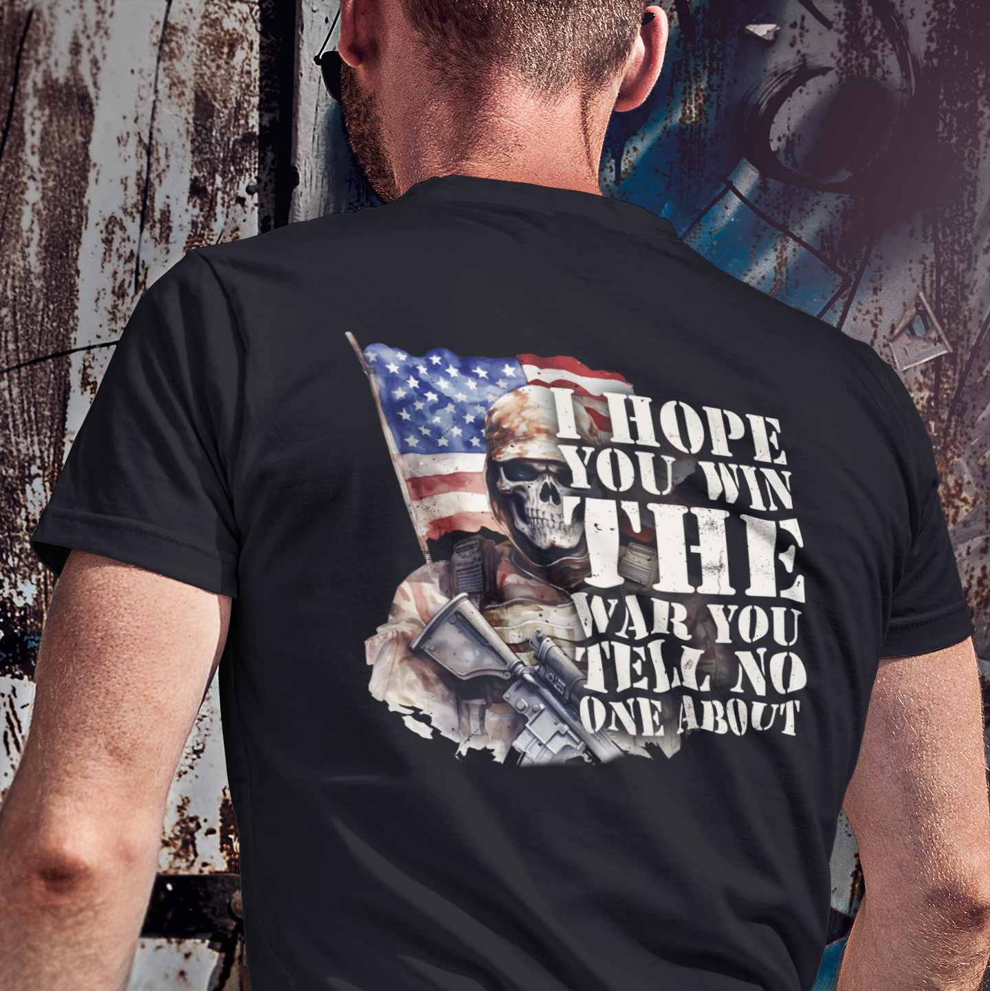 Person wearing a black t-shirt with graphic design and text, standing against a textured wall.