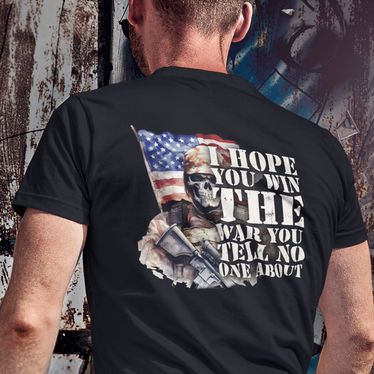 Person wearing a black t-shirt with graphic design and text, standing against a textured wall.