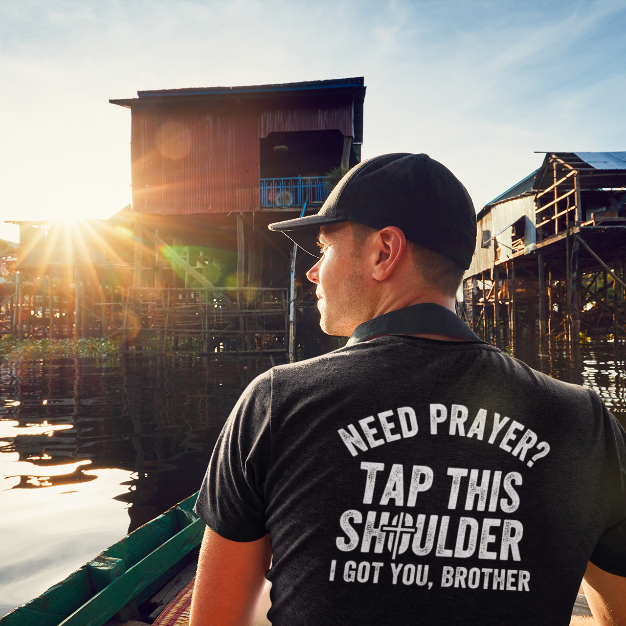 Man on a boat with text on his shirt near stilt houses on water