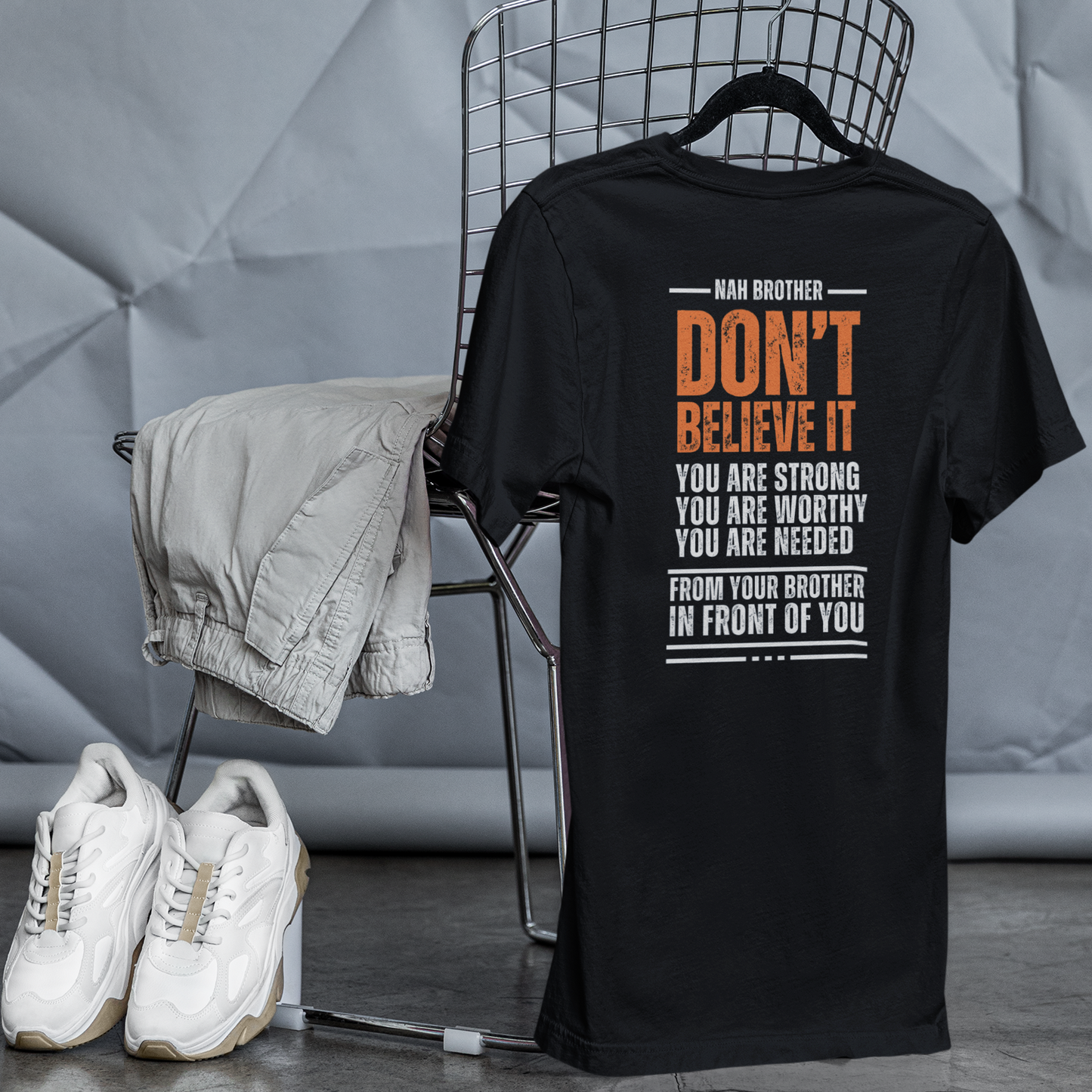 Black t-shirt with text on a chair against a textured gray wall.