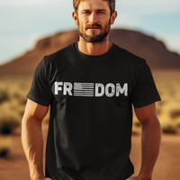 Man wearing a black t-shirt with 'Freedom' printed on it, standing in a desert landscape.