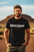 Man wearing a black t-shirt with 'Freedom' printed on it, standing in a desert landscape.